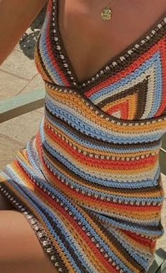 a woman wearing a multicolored crochet swimsuit holding a cell phone