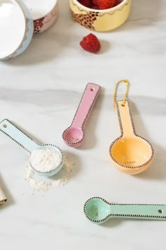 three measuring spoons and two bowls with strawberries in them