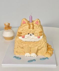 a cake shaped like a cat sitting next to a cupcake with a candle on it