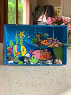 a blue box filled with colorful fish on top of a counter next to flowers and seashells