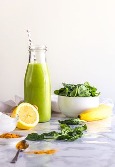 a green smoothie in a glass bottle, surrounded by other fruits and vegetables on a marble table