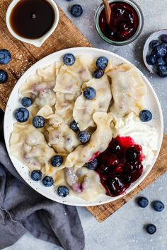 a bowl filled with dumplings covered in blueberries and sauce next to two cups of coffee