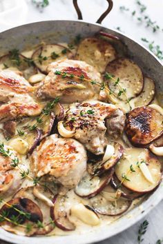 a skillet filled with chicken, potatoes and onions on top of a white table