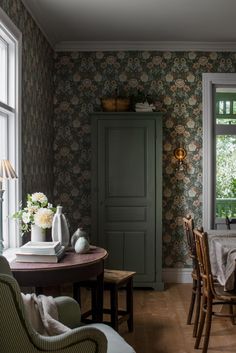 a dining room table and chairs in front of a green cabinet with flowers on it