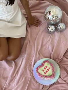 a woman in white dress sitting on bed next to cake and disco ball decorations with pink sheets