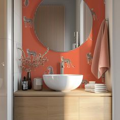 a bathroom with an orange wall and white bowl sink in front of a round mirror that has giraffes on it