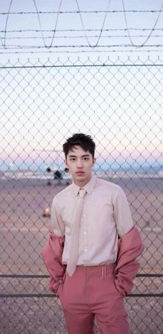 a young man standing in front of a fence with his hands on his hips and looking at the camera