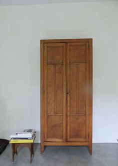 an old wooden armoire next to a small table with books on it in a room