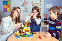 three children and an adult playing with wooden blocks at a table in a school room