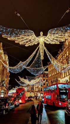 people walking down the street with christmas lights strung all around them and an angel statue