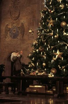 a man standing next to a christmas tree in front of a large wall with gold decorations