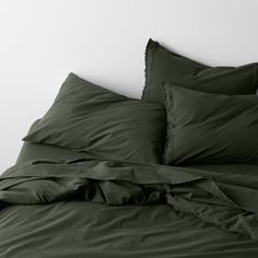 an unmade bed with dark green sheets and pillowcases on top of it