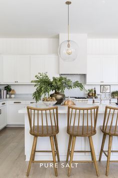 three wooden chairs sitting in front of a white kitchen island with two plants on it