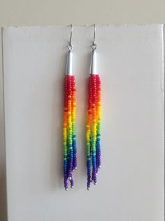 two pairs of multicolored beads hanging from silver earwires on a white surface