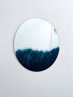 a round mirror hanging on the side of a white wall with blue water in it