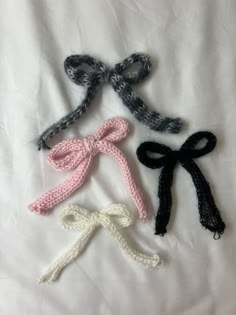 three knitted bows laying on top of a white sheet with black and pink ribbons