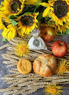 an arrangement of sunflowers, apples and cookies on a table with wheat stalks