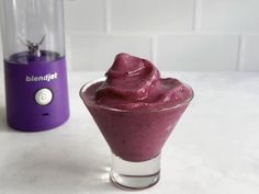 a purple smoothie in a glass next to a blender on a white counter