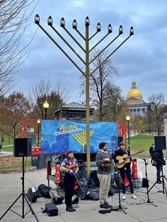 a group of people playing music in front of a large blue sign with the words happy hanukkah written on it