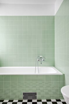 a green tiled bathroom with a white bathtub and black and white checkered floor