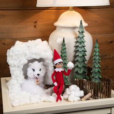 an elf is standing in front of a fake snowman and polar bear with trees