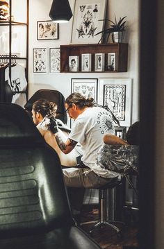 a man is getting his hair cut by another person in the room with pictures on the wall