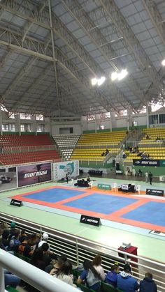 an indoor tennis court with people sitting on the benches and watching something in the distance