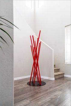 a tall red sculpture sitting on top of a wooden floor next to a stair case