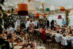 a group of people sitting at tables in a tent with lights hanging from the ceiling