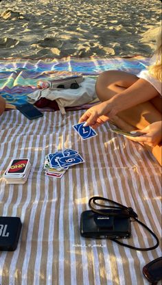 a woman sitting on top of a beach towel next to a bag and cell phone