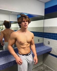 a shirtless man standing in front of a blue and white tiled bathroom counter top