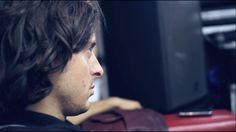 a man with long hair sitting in front of a red suitcase and looking off into the distance