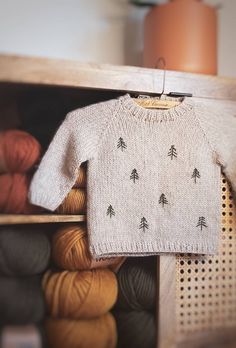 a knitted sweater hanging on a rack with balls of yarn in front of it