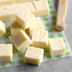 several pieces of cheese on a green and white checkered tablecloth with a wooden utensil in the background