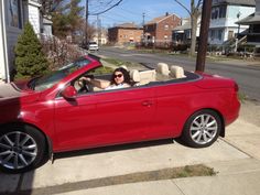 a woman sitting in the driver's seat of a red convertible car on a residential street