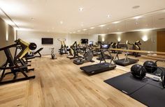 there are many exercise machines in this gym room with hard wood flooring and mirrors on the wall