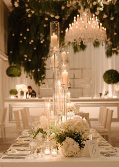 a long table with candles and flowers on it in front of a chandelier