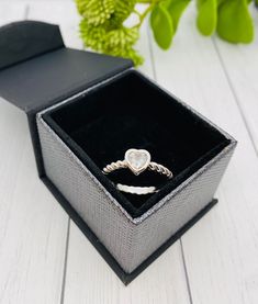 an open box with a ring inside on a white wooden table next to a green plant