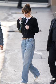 a woman walking down the street wearing high waist jeans and a black cardigan sweater