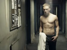 a shirtless man is standing in the hallway with his hand on his hip and looking at the camera