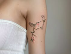 a woman's arm with a small bird and flower tattoo on the left side of her arm