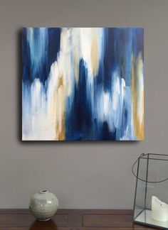 an abstract painting hangs on the wall above a wooden table with a vase and candle