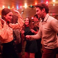 two people dancing at a party with other people in the back ground and lights on