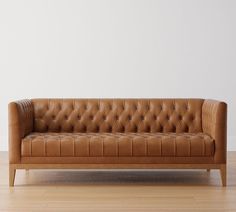 a brown leather couch sitting on top of a hard wood floor next to a white wall