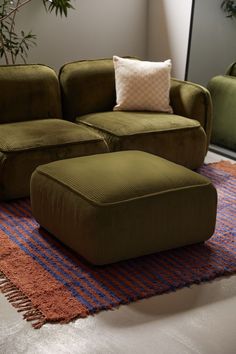 a large green couch sitting on top of a rug next to a chair and ottoman