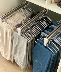 an organized closet with clothes hanging on rails and folded jeans in the foreground, next to a mirror