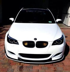 a white car is parked in front of a garage with its hood up and lights on