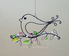 a bird hanging from a wire with flowers and leaves on it's back end