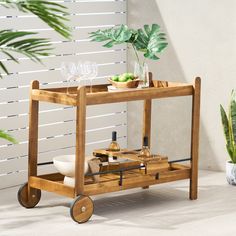 a wooden serving cart with wine glasses and bottles on it next to a potted plant