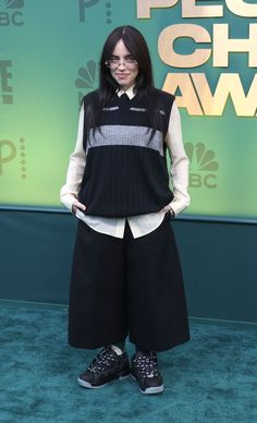 a woman standing in front of a green wall wearing black and white clothing with her hands on her hips